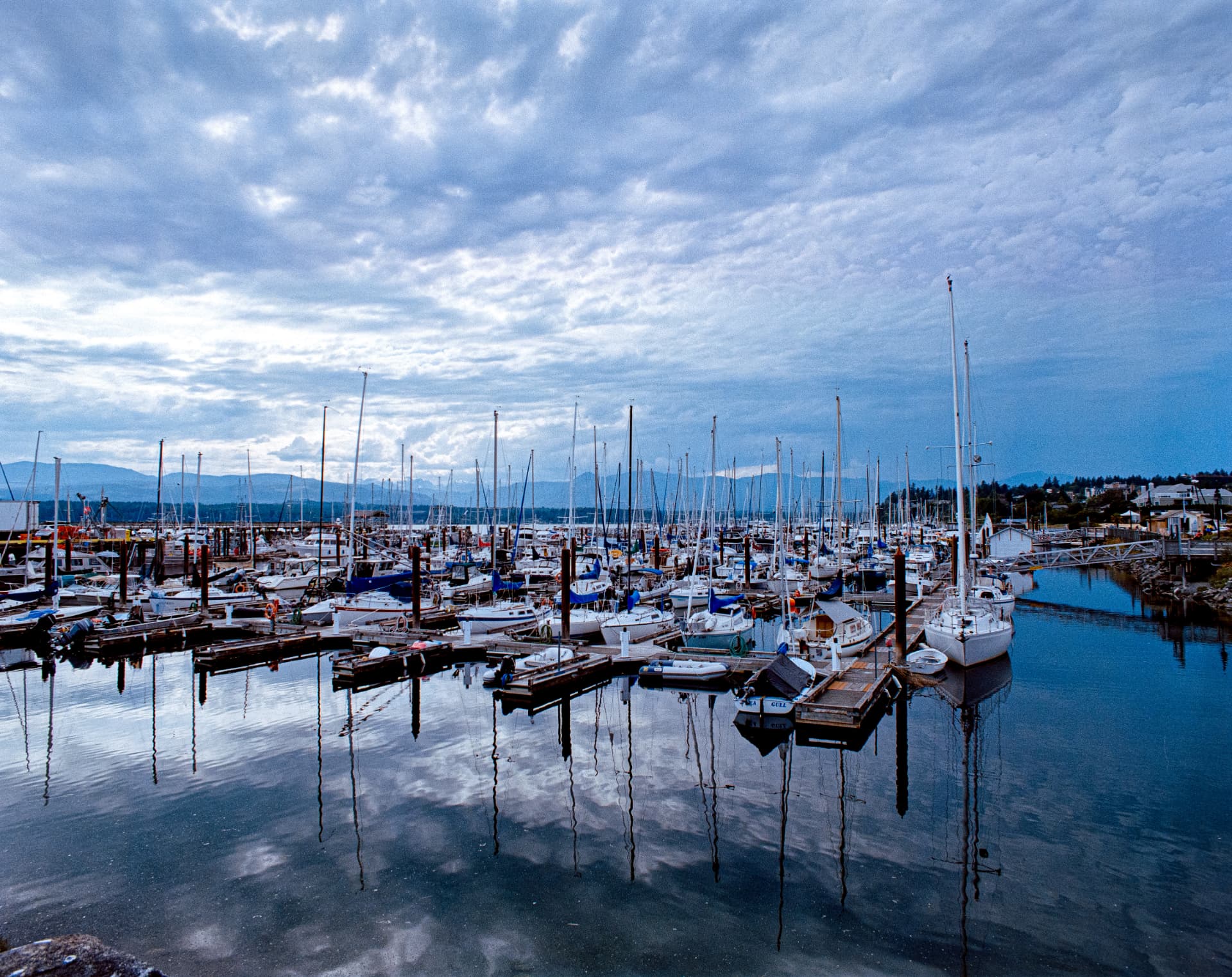 Marina — moored sailboats and masts reflected in still water under a clouded sky