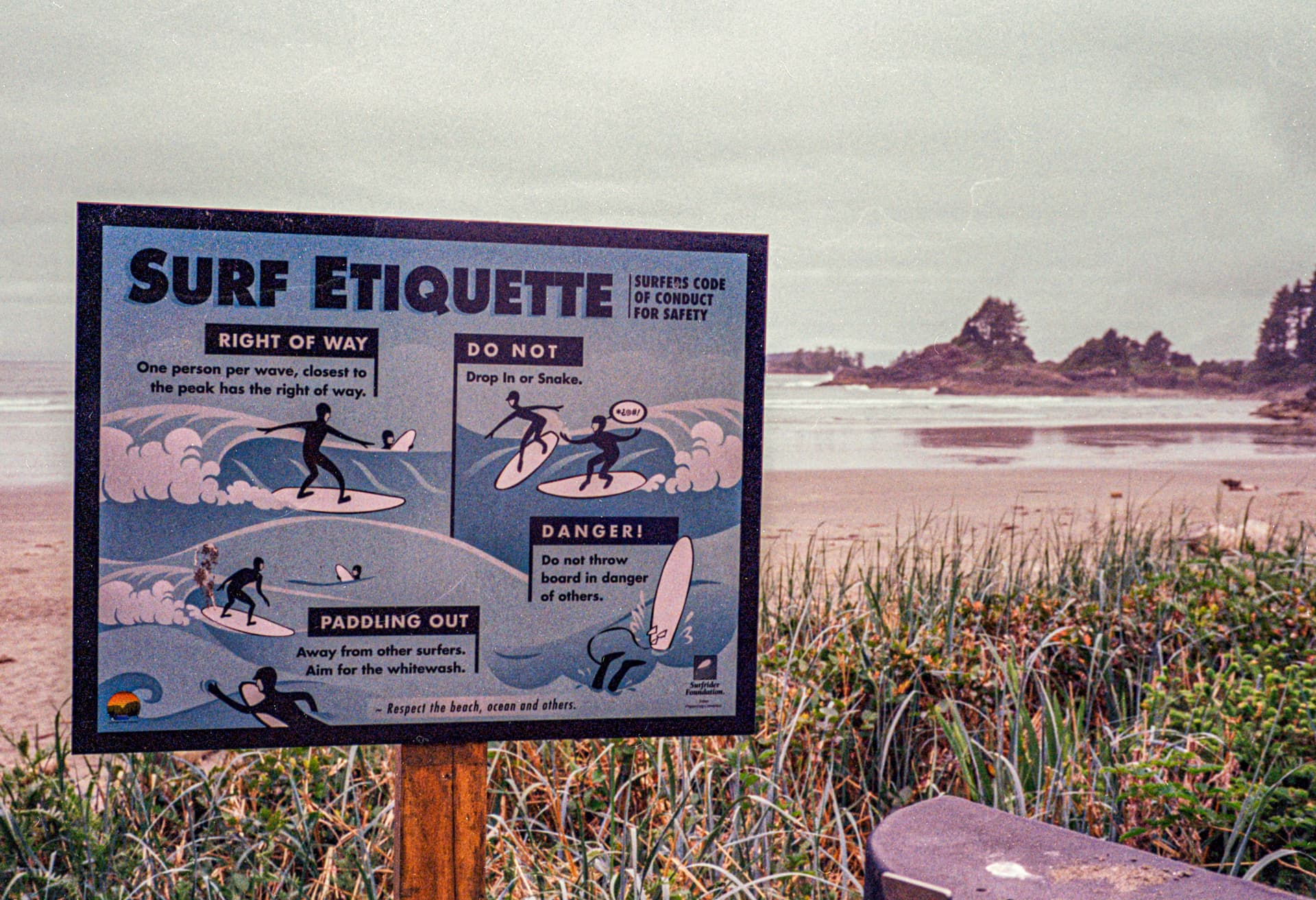 Surf Etiquette — a beach sign above dune grass with a headland in the distance
