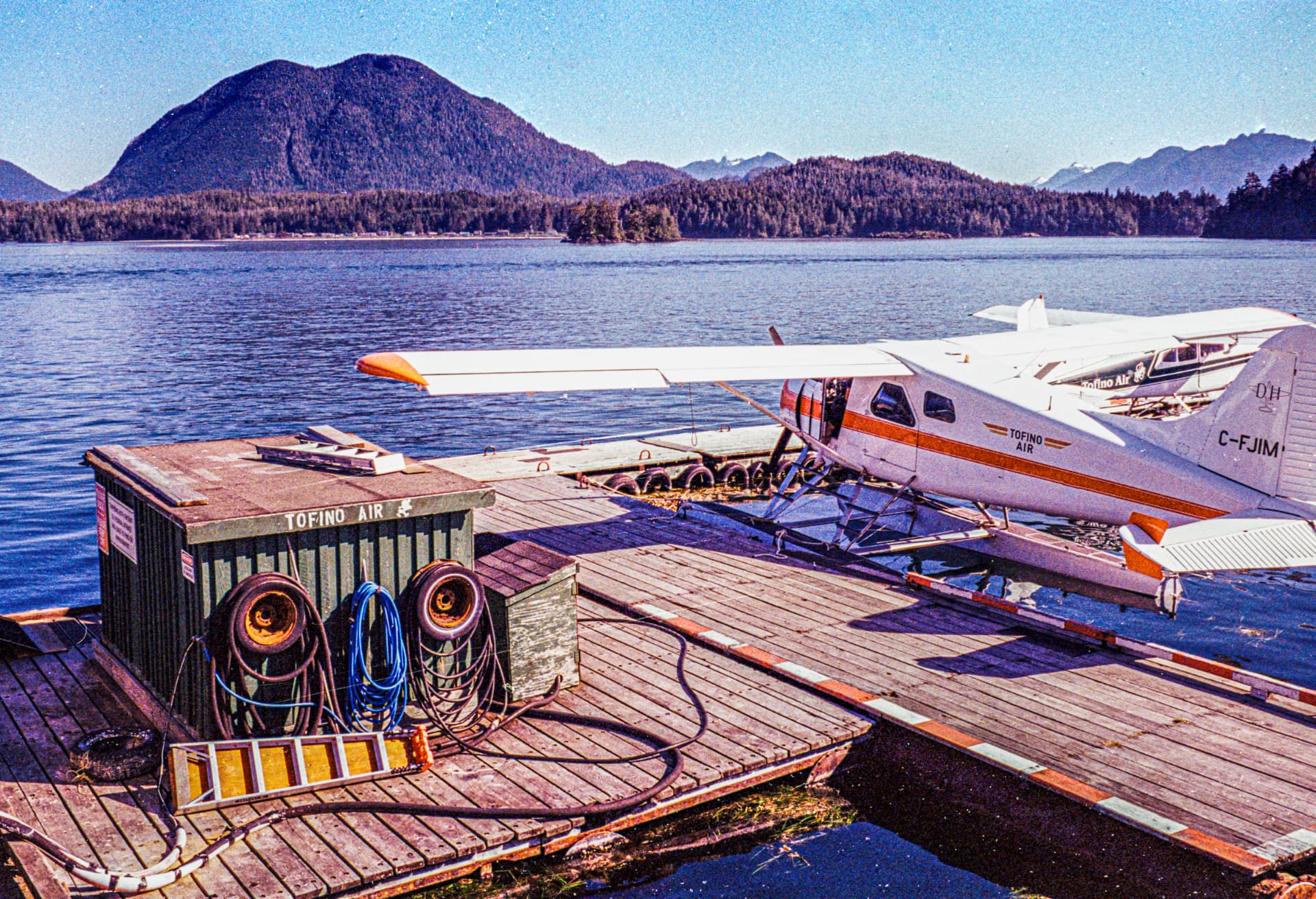 Tofino Air — a float plane tied to a wooden dock with mountains beyond