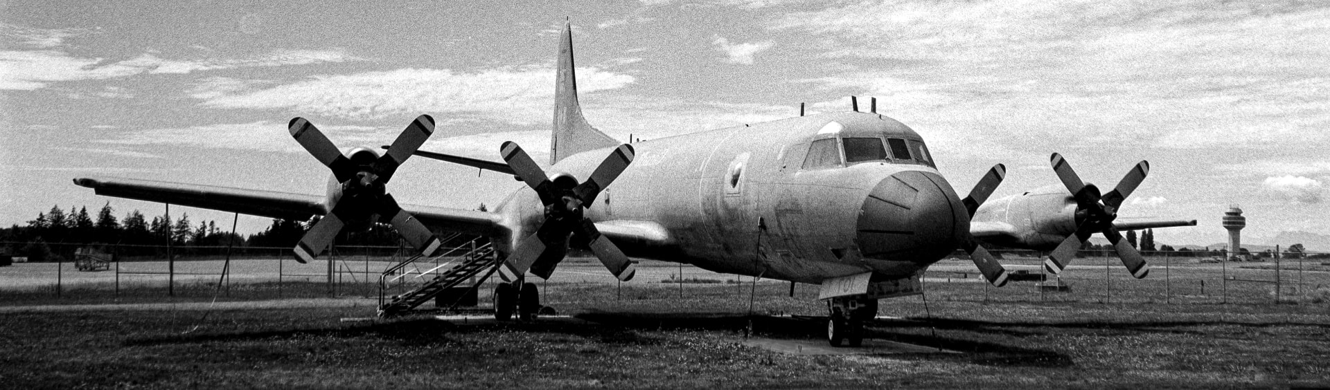 A parked four-propeller Aurora patrol aircraft on an airfield in panoramic frame